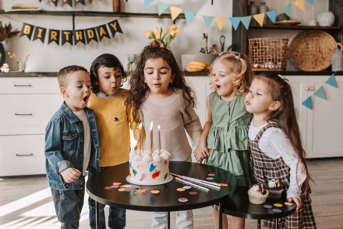 Crianças em volta do bolo assoprando as velinhas numa festa de aniversário em casa